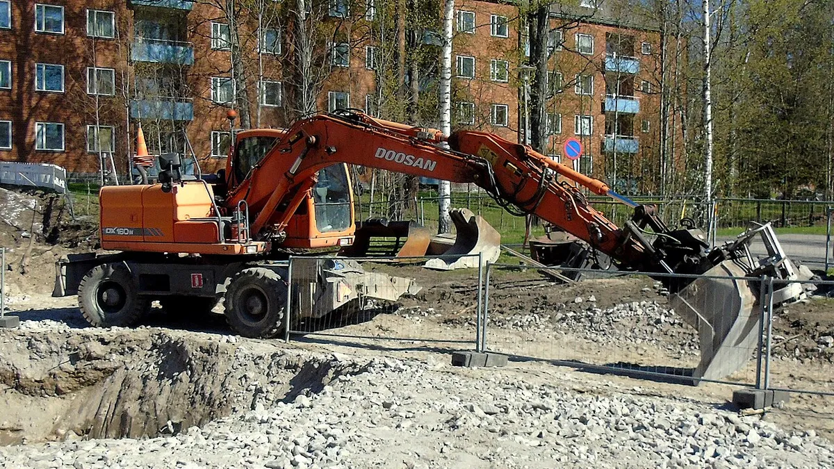 Колёсный экскаватор Doosan DX160W прошлого поколения, выпущенный до смены бренда на Develon, копает траншею во дворе